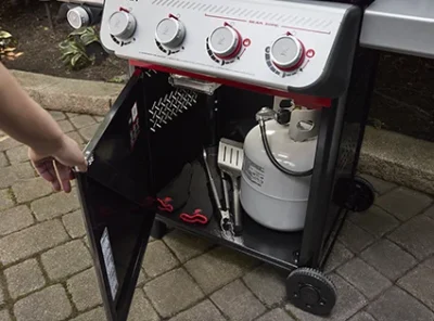 Weber Spirit® E-310 - Szafka z drzwiczkami skrywa butlę na propan i akcesoria do grillowania.